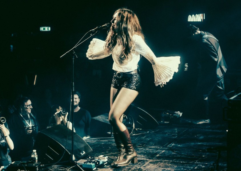 A woman performing on stage wearing black sequinned shorts and a white bell sleeve lace topx